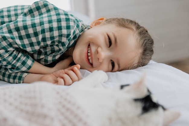 Una niña rubia con pijama abraza a un gato doméstico en su dormitorio el concepto de una acogedora mañana en casa