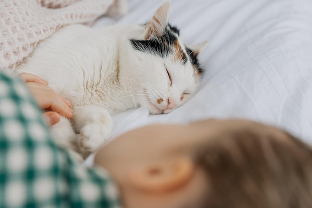 Una niña rubia con pijama abraza a un gato doméstico en su dormitorio el concepto de una acogedora mañana en casa