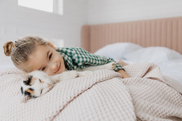 Una niña rubia con pijama abraza a un gato doméstico en su dormitorio el concepto de una acogedora mañana en casa