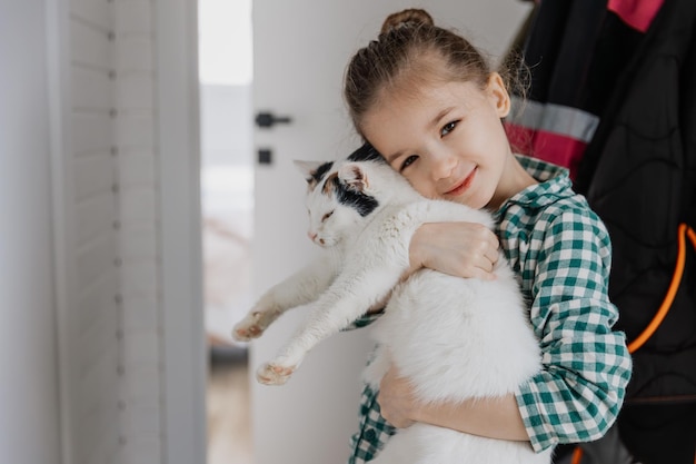 Una niña rubia con pijama abraza a un gato doméstico en su dormitorio el concepto de una acogedora mañana en casa