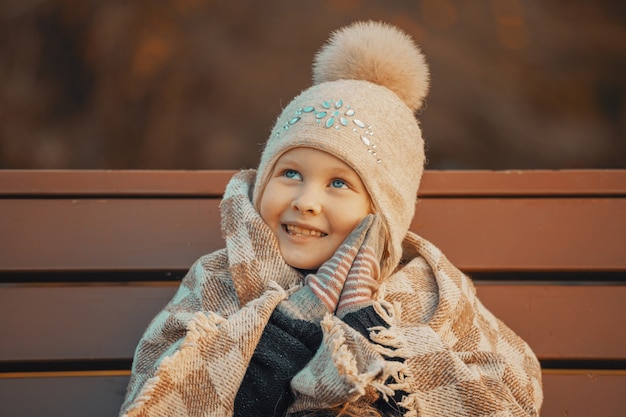 Niña rubia en un plaid en el parque en un banco