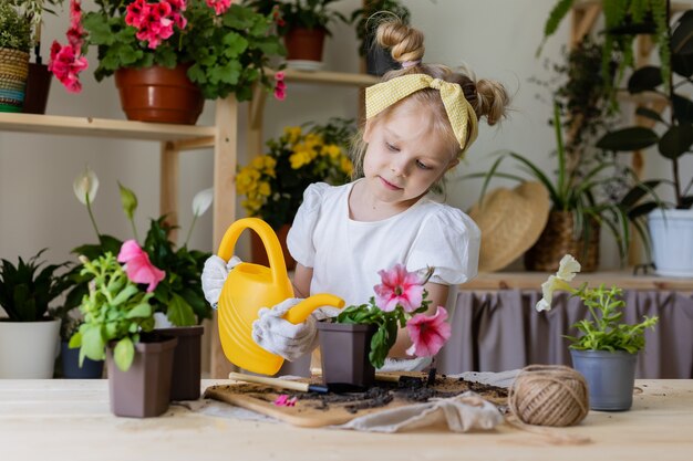 niña rubia plantas y trasplantes y riega flores de interior Pequeño ayudante por tareas