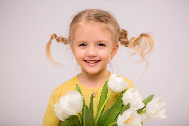 Niña rubia con un ramo de tulipanes sobre un fondo claro