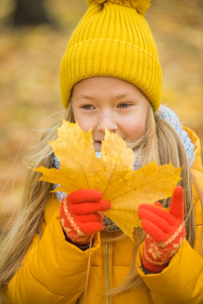 Foto niña rubia en ropa amarilla con hoja amarilla, otoño