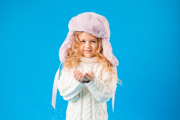 niña rubia en ropa de invierno sopla la nieve de sus manos