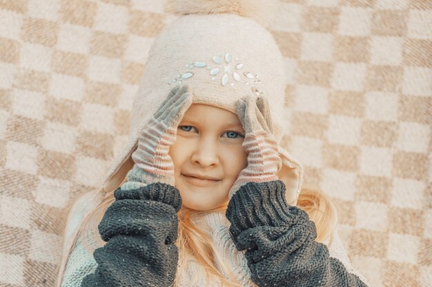 Niña rubia con un sombrero de lana en un plaid en el parque