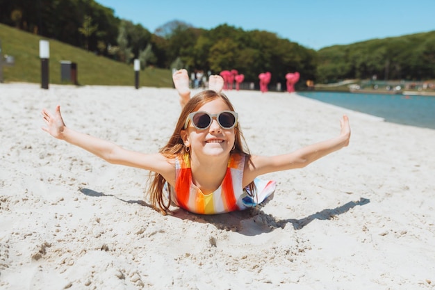 Una niña rubia con un sombrero de paja yace en una playa de arena chica tomando el sol en la arena