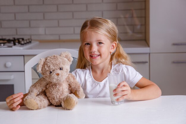 Niña rubia sonriente bebiendo leche en la cocina