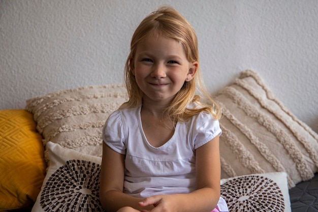 Foto niña rubia sonriente en camiseta sentada en el sofá