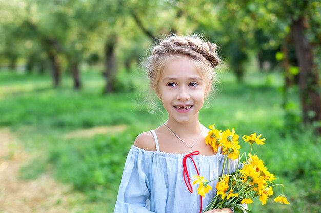Niña rubia sonriente con un ramo de flores amarillas niño en el jardín de verano