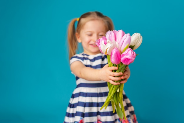 Niña rubia sonriente con ramo de tulipanes sobre fondo azul