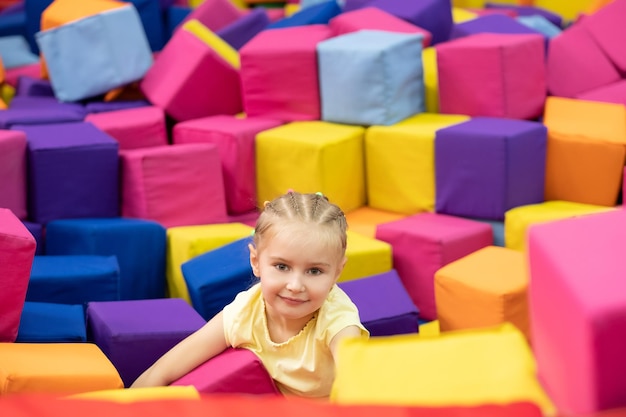 Niña rubia sonriente sentada en la sala de juegos con coloridos cubos suaves