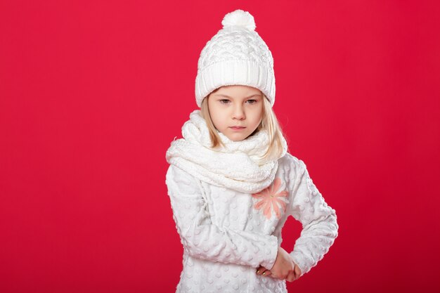 Niña rubia sonriente en un sombrero blanco y bufanda en rojo