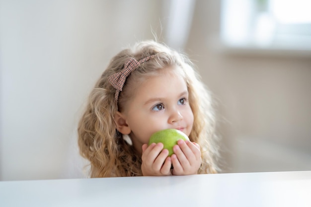 Niña rubia sosteniendo una manzana en casa Foto de alta calidad