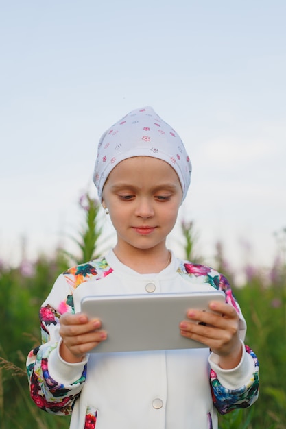 Niña rubia con tableta digital en la naturaleza