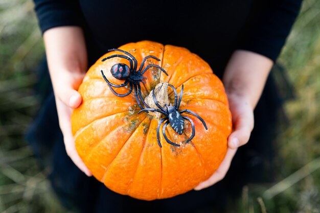 Niña rubia con un traje negro, halloween con una calabaza en sus manos, primer plano.