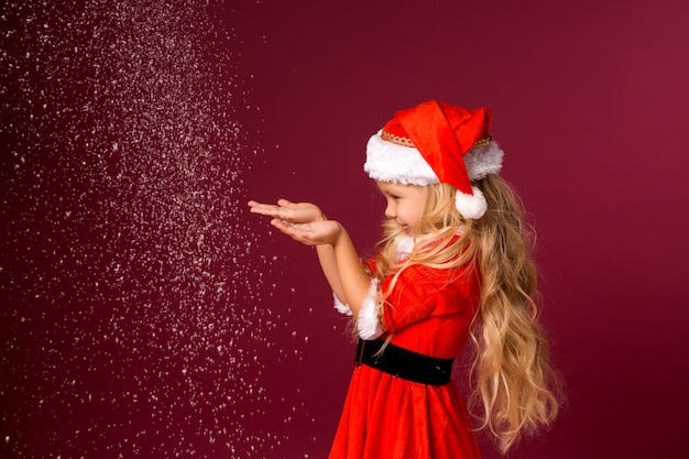 Niña rubia en traje de Santa atrapa nieve