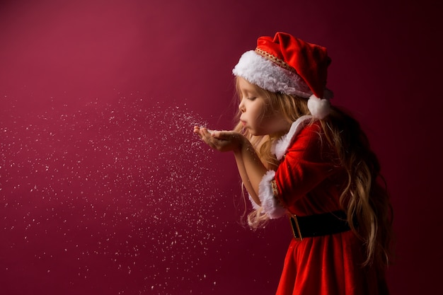 niña rubia en un traje de Santa sopla nieve de sus manos