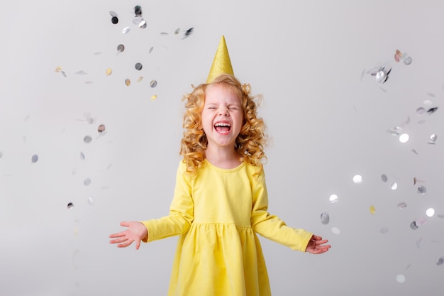 Niña rubia con un vestido amarillo atrapa confeti sonriendo feliz con fondo blanco