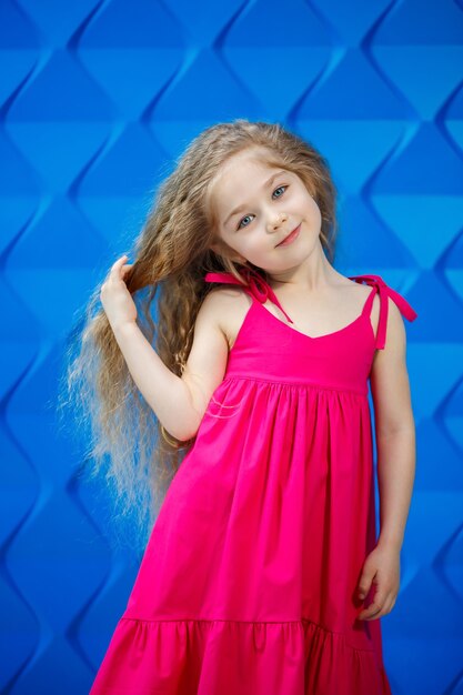 Niña rubia con un vestido rosa sobre un fondo azul bailando y riendo, las emociones de alegría de los niños brillantes, infancia feliz