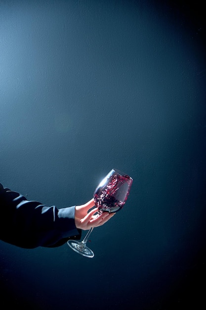 Foto la niña está sacudiendo una copa de vino tinto en la mano sobre un fondo azul.