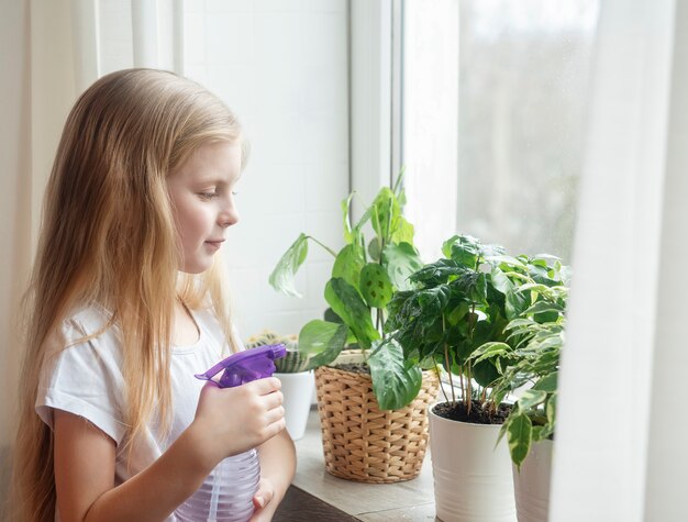 Niña salpicando agua sobre las plantas de la casa