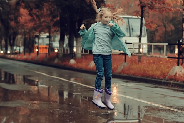 niña saltando en los charcos bajo la lluvia de otoño