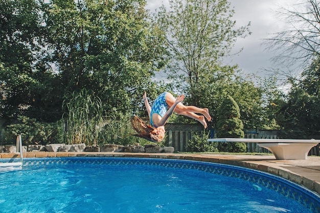 Foto niña saltando en la piscina contra los árboles