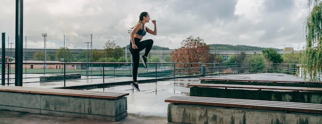 Niña saltando sobre bancos haciendo entrenamiento al aire libre en días lluviosos