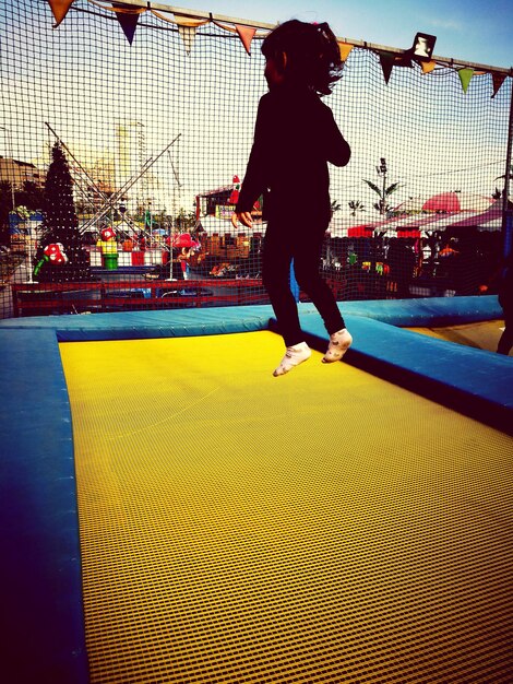 Foto niña saltando en trampolín contra el cielo