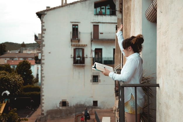 Foto niña saluda desde su balcón mientras sostiene un libro