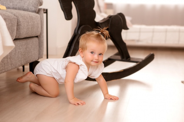 Niña sana en una habitación junto a un sofá gris está aprendiendo a caminar