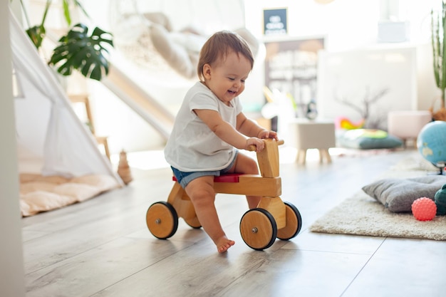 Foto niña en un scooter de madera en la habitación de los niños