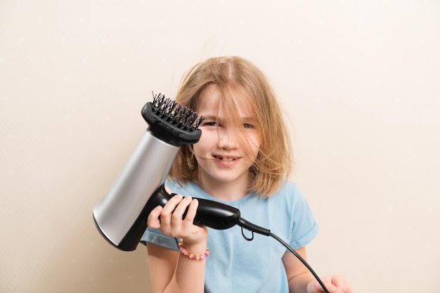 La niña se seca el pelo con un secador de pelo con un accesorio de peine