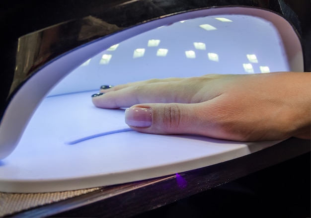 La niña se seca las uñas en una lámpara después de aplicar esmalte en gel.