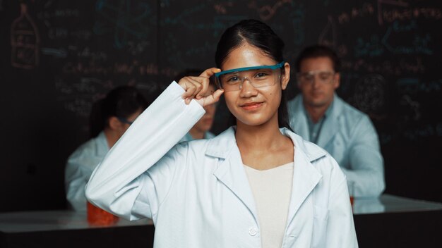 Niña de secundaria mirando a la cámara mientras la gente hace un experimento Edificación