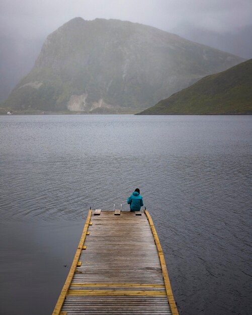 niña sentada al final de un muelle durante la niebla en un fiordo noruego en las islas lofoten