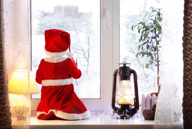 Niña sentada en el alféizar de una ventana con un traje de Santa Claus