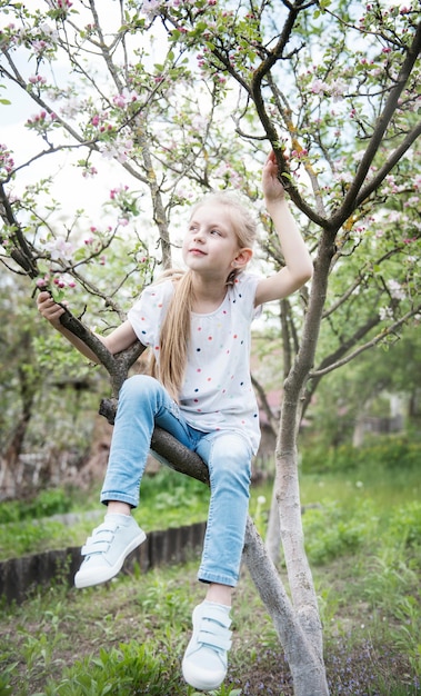 Niña sentada en el árbol floreciente en el jardín de la manzana