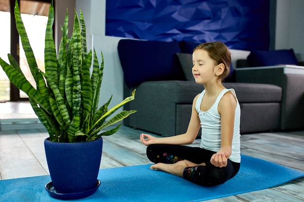 Una niña sentada en asanas de yoga en un azul.