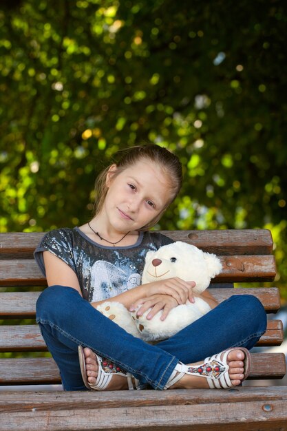 Niña sentada en un banco con osito en el parque