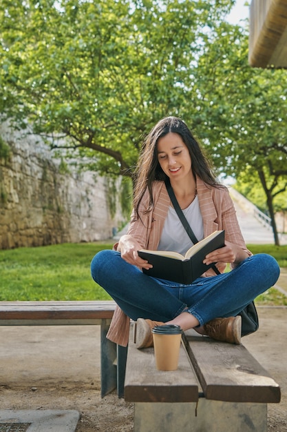 Niña sentada en un banco en el parque leyendo un libro