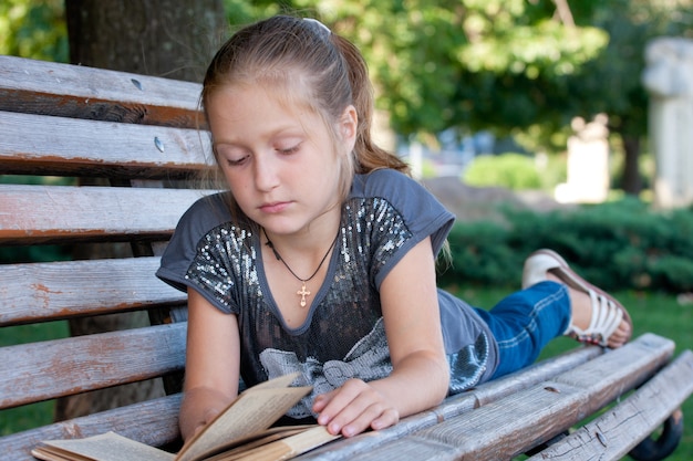 Niña sentada en un banco en el parque y leyendo.