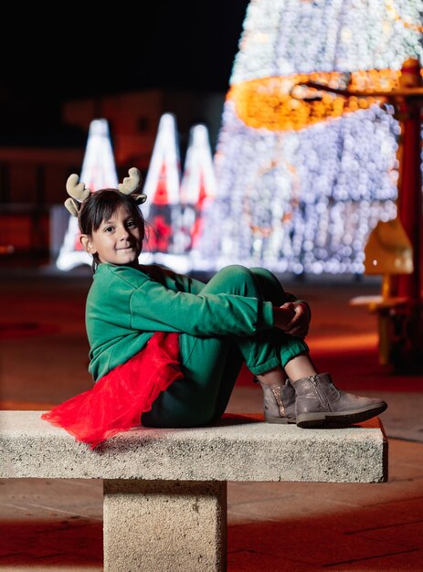 Niña sentada en un banco con vestido navideño con cuernos de reno