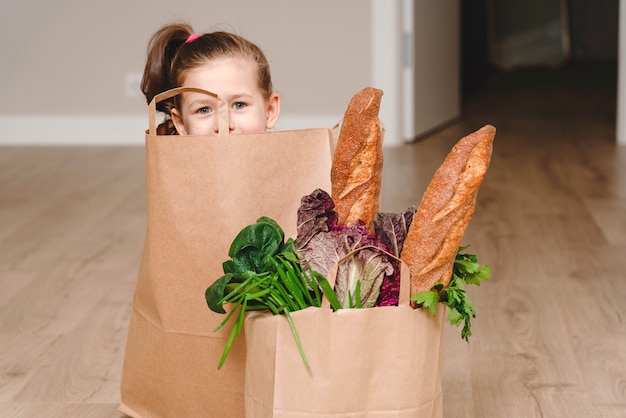 Niña sentada en una bolsa de papel escondido con verduras y pan, comestibles con espacio de copia