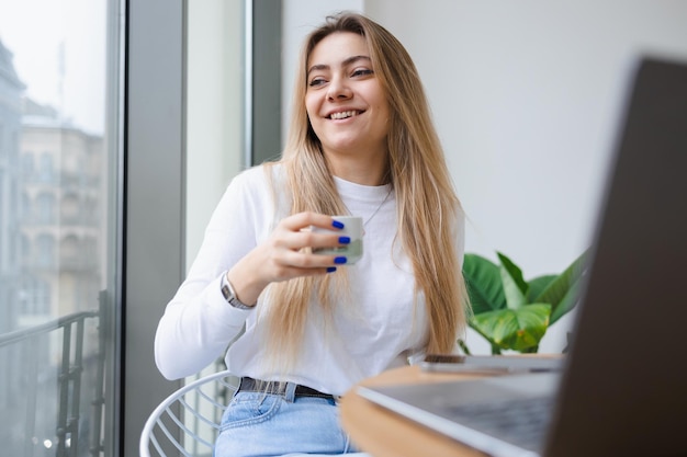 Niña sentada en un café bebe café entre el trabajo en una computadora portátil