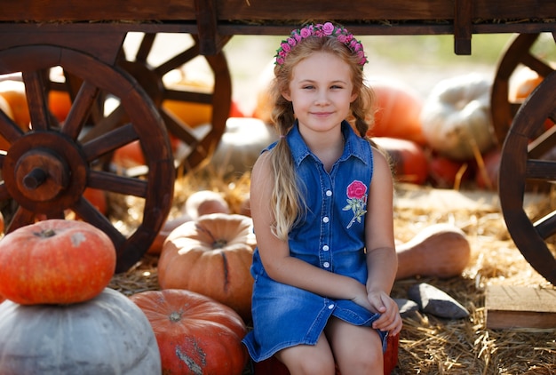 Niña sentada entre calabazas en el mercado de agricultores local en un día soleado de otoño.