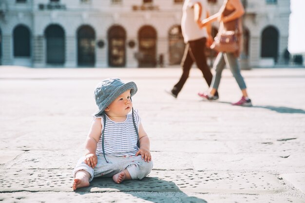 Niña sentada en una calle de la ciudad europea y apuntando con el dedo hacia arriba Niño pequeño al aire libre en una ciudad