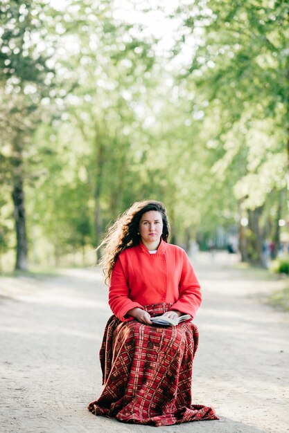 Niña sentada en el camino con la manta y el libro en las piernas.