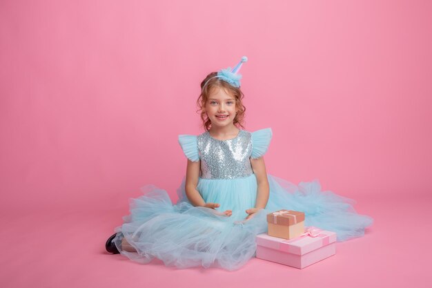 niña sentada celebrando cumpleaños con fondo rosa, hermoso vestido de princesa